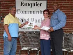Celia and Mack Webb present books from an anonymous donor to Roland Serrano, Fauquier Community Food Bank Director.